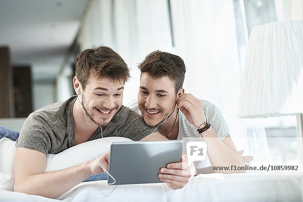 Homosexual couple lying in bed with tablet