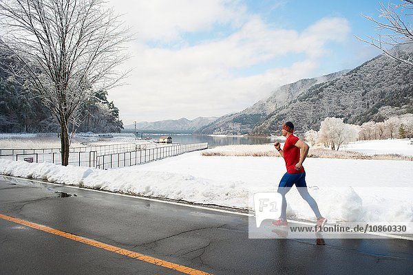 Männlicher Läufer  der im Winter entlang der Straße läuft  Kawaguchiko-See  Berg Fuji  Japan