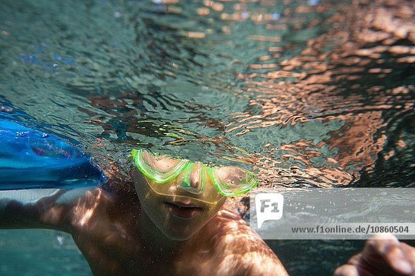 Unterwasseraufnahme eines Jungen mit Unterwasser-Brille  der unter Wasser schwimmt