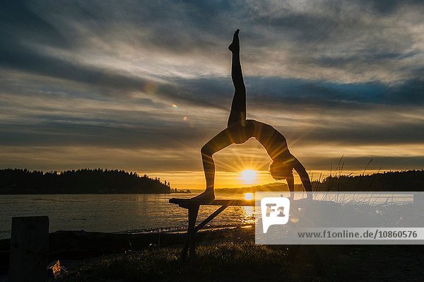 Frau praktiziert Yoga am See bei Sonnenuntergang