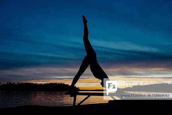 Frau praktiziert Yoga am See bei Sonnenuntergang