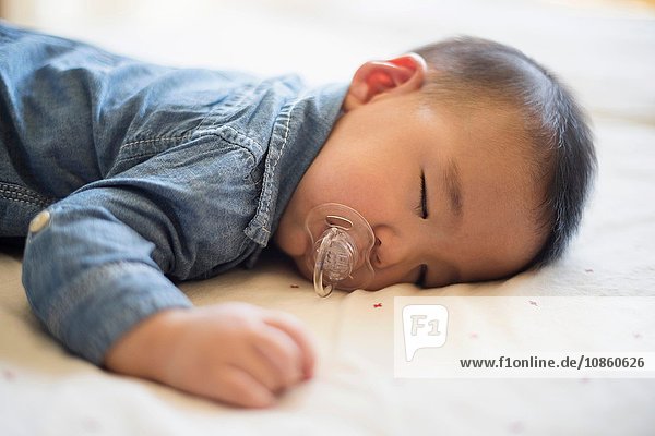 Baby boy with pacifier sleeping on bed