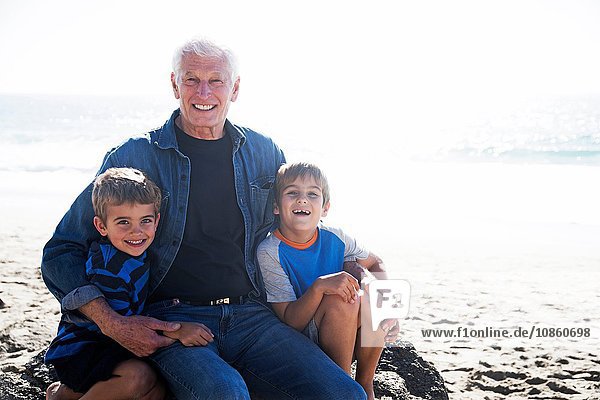 Großvater mit zwei Enkeln  am Strand sitzend  lächelnd