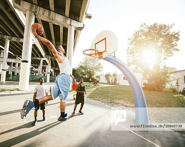 Side view of young man on basketball court holding basketball jumping for hoop