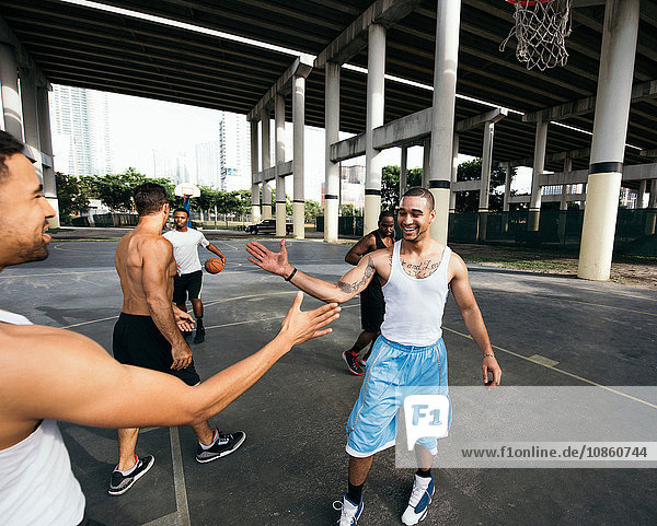Young men on basketball court connecting with handshake after basketball game smiling