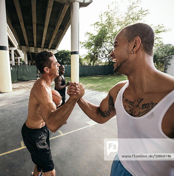 Men on basketball court connecting with handshake after basketball game smiling