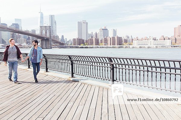 Männliches Paar beim Spaziergang am Flussufer bei der Brooklyn Bridge  New York  USA