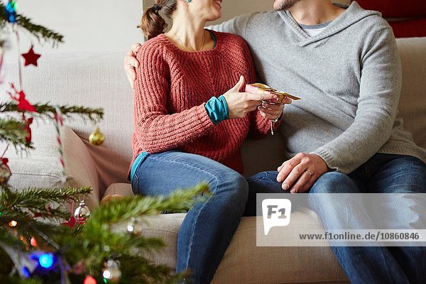 Paar überreicht Weihnachtsgeschenke auf Wohnzimmer-Sofa