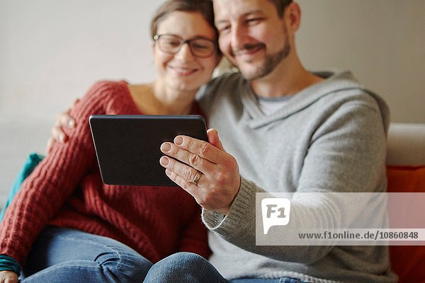 Mittelgroßes  auf dem Sofa sitzendes Paar  das sich mit einem digitalen Tablett selbstständig macht