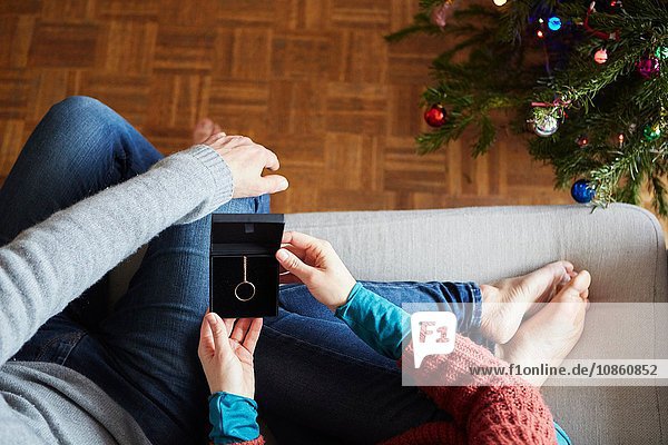 Overhead view of couple holding xmas necklace gift on living room sofa