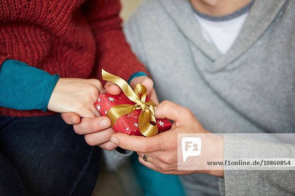 Close up of couple holding hands and xmas gift on sofa