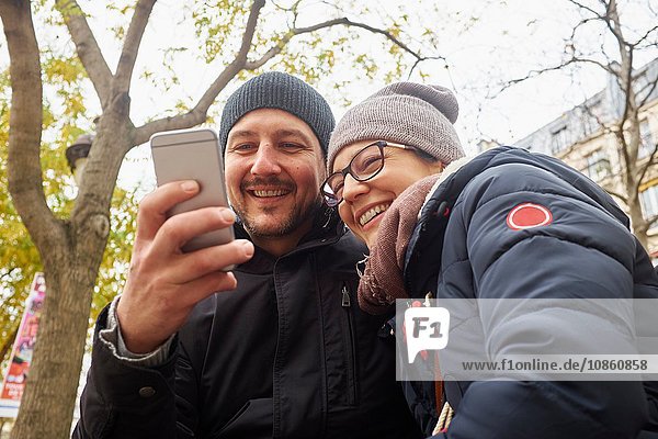 Paar mit Strickmützen im Park beim Lesen von Smartphone-Texten
