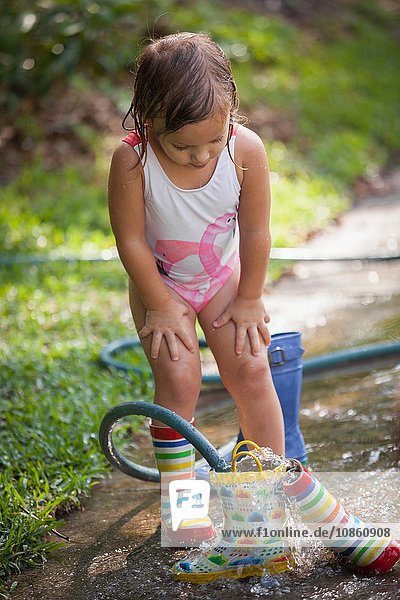 Child filling wellies with water from hose