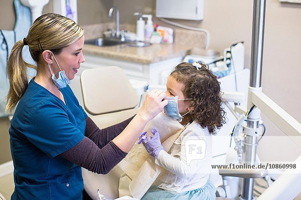 Lächelnde Seitenansicht eines Mädchens und eines Zahnarztes in einer Zahnarztpraxis mit chirurgischen Masken