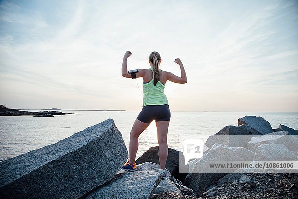 Rear view of woman standing on rocks arms raised flexing muscles