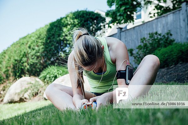 Frau mit Aktivitätsspürgerät auf Gras sitzend  sich streckend und nach unten blickend