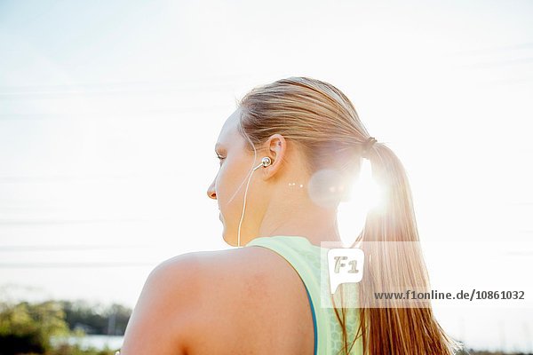 Low angle rear view of woman with ponytail wearing earbuds looking away