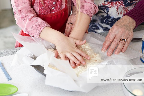 Hände eines Mädchens und einer Großmutter  die Kuchenteig an der Küchentheke verteilen