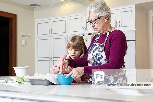 Mädchen und Großmutter mischen Kuchen an der Küchentheke