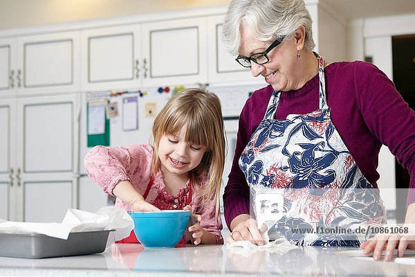 Mädchen und Großmutter mischen Kuchen in einer Schüssel an der Küchentheke