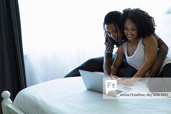 Lesbisches Paar sitzt im Bett und schaut auf den Laptop