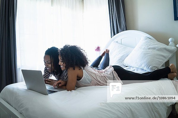 Lesbian couple lying on bed  using laptop
