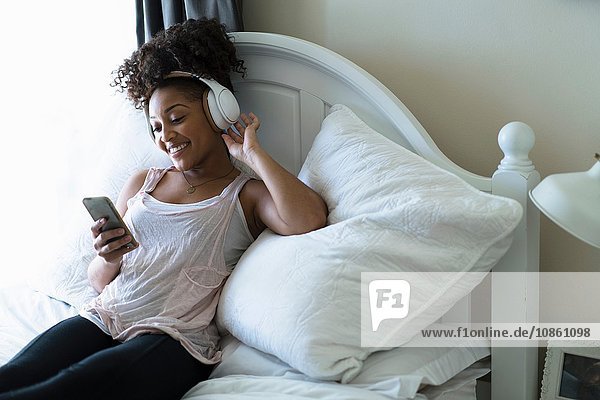 Frau entspannt sich im Bett  trägt Kopfhörer  schaut auf Smartphone