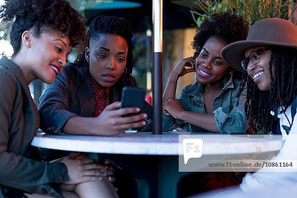 Gruppe von Freundinnen  die am Tisch sitzen und auf ein Smartphone schauen  im Freien