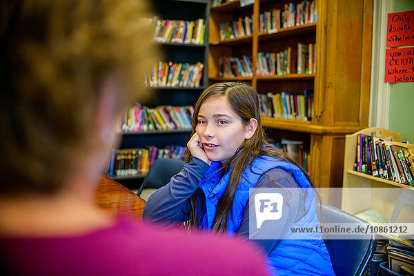 Teenager-Mädchen mit Hand am Kinn  in der Schulbibliothek im Gespräch mit Berufsberater