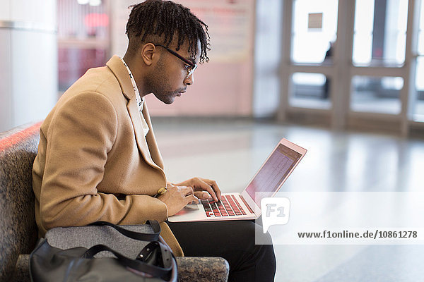 Young businessman sitting in train station typing on laptop