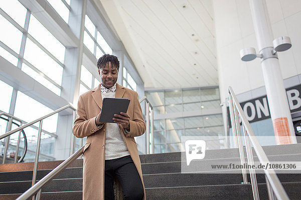 Junger Geschäftsmann mit digitalem Tablet bewegt sich die Bahnhofstreppe hinunter
