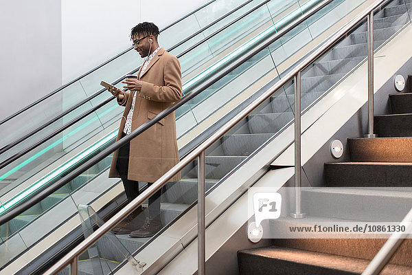 Young businessman moving down train station escalator reading smartphone