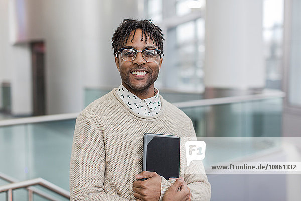 Portrait of happy young businessman standing in train station holding digital tablet