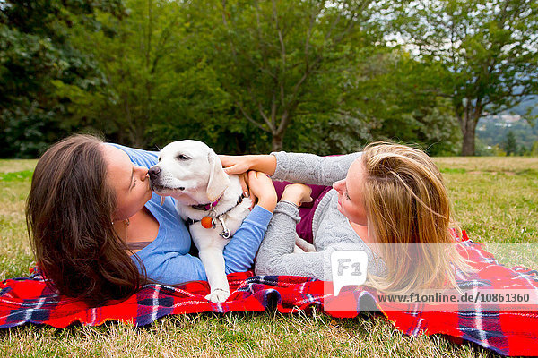 Two young women with pet dog  lying on blanket in park