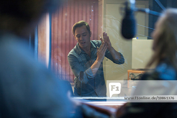 Musiker im Aufnahmestudio  Musikproduzent  der mit ihnen durch ein Fenster kommuniziert