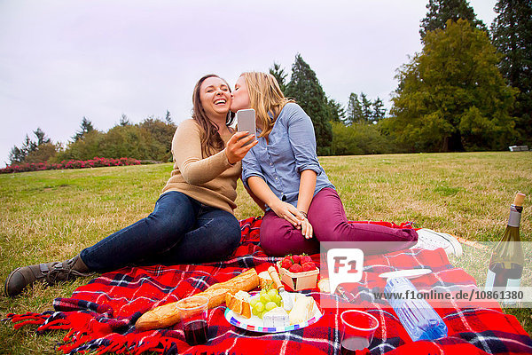 Zwei junge Frauen beim Picknick im Park  beim Herumalbern  beim Selbermachen  mit dem Smartphone