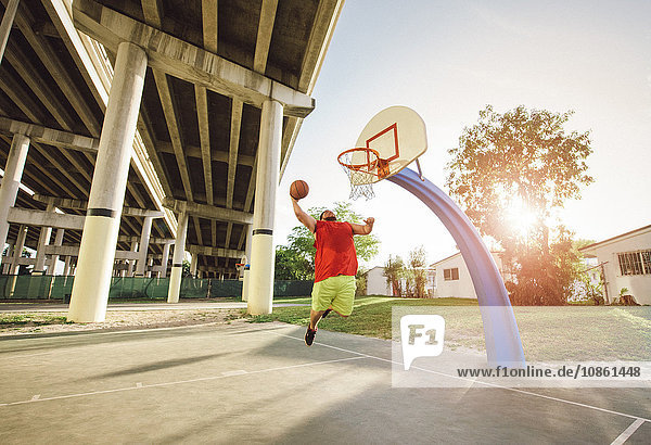 Low angle view of man on basketball court in mid air jumping for basketball hoop