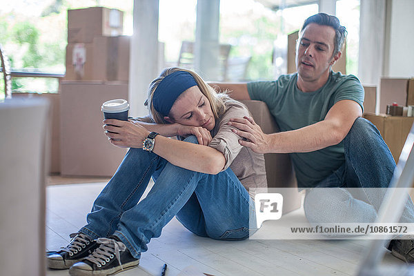 Moving house: Couple taking a break  sitting in room filled with cardboard boxes