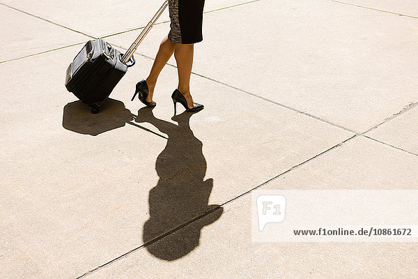 Geschäftsfrau  die im Freien geht  hochhackige Schuhe trägt  Koffer mit Rädern zieht  niedriger Abschnitt