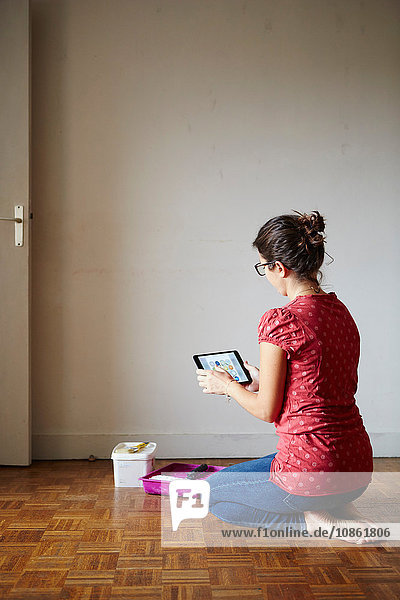Frau kniend neben Dekorationsgeräten  Blick auf digitales Tablett  Rückansicht
