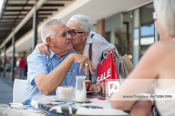 Shopperin küsst älteren Mann im Straßencafé auf die Wange