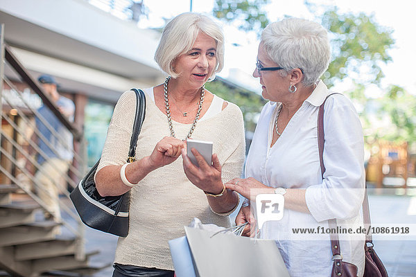 Ältere Käuferinnen lesen Smartphone-Texte im Einkaufszentrum