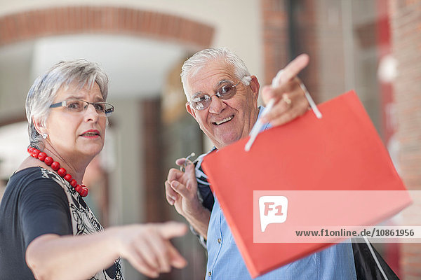 Mature couple walking along street  carrying shopping bags  pointing behind them