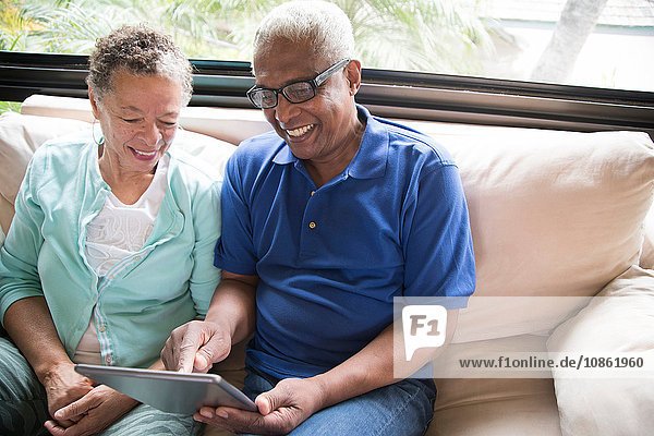 Älteres Ehepaar sitzt auf dem Sofa und benutzt ein digitales Tablett
