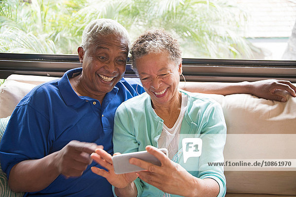 Älteres Ehepaar sitzt auf dem Sofa  schaut auf das Smartphone  lacht