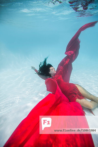 Frau in rotem Kleid  mit rotem Stoff drapiert  schwimmt unter Wasser