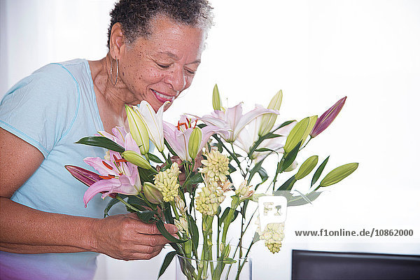 Ältere Frau riecht Vase mit Blumen und lächelt
