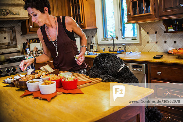 Frau bereitet Snacks an der Küchentheke vor und wird von einem Hund beobachtet