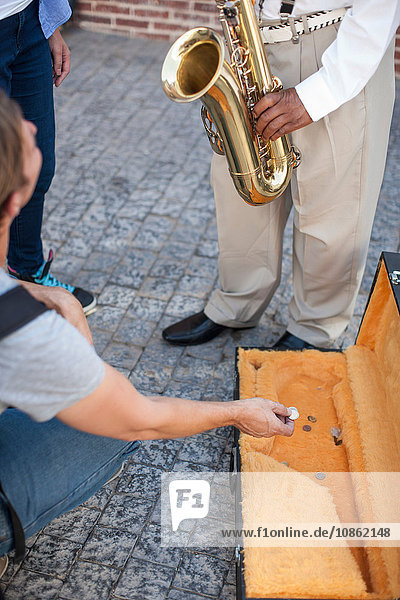 Fußgänger wirft Geld in den Musikkoffer eines Straßenmusikers,  niedriger Abschnitt