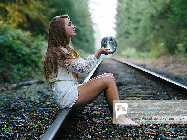 Teenagerin  sitzt auf einem Bahngleis und hält eine Kristallkugel